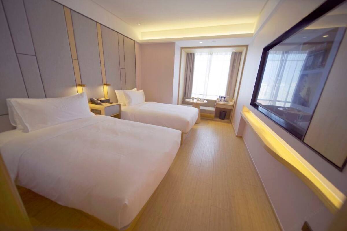 Una habitación de hotel con dos camas, una mesita, una silla, una ventana y un televisor.