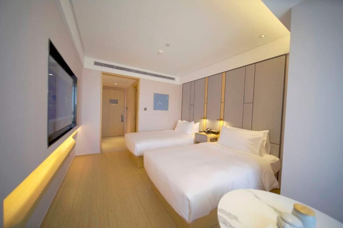 Habitación de hotel con dos camas, televisión, mesita de noche con lámpara y suelo de madera.