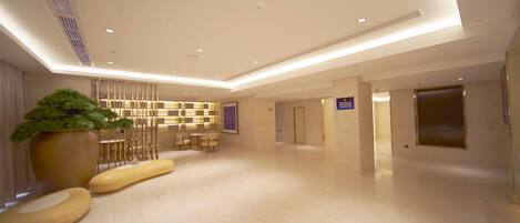 A spacious lobby with a reception desk, seating area, and a large potted plant.
