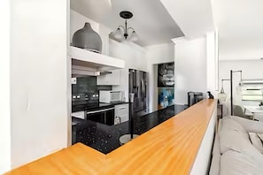 A modern kitchen with a wooden countertop, white cabinetry, and a black backsplash. - Private Oasis Bungalow (Orlando)