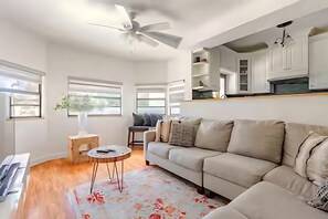 A modern living room with a beige sofa, a round coffee table, a ceiling fan, and a kitchen area with white cabinets. - Private Oasis Bungalow (Orlando)