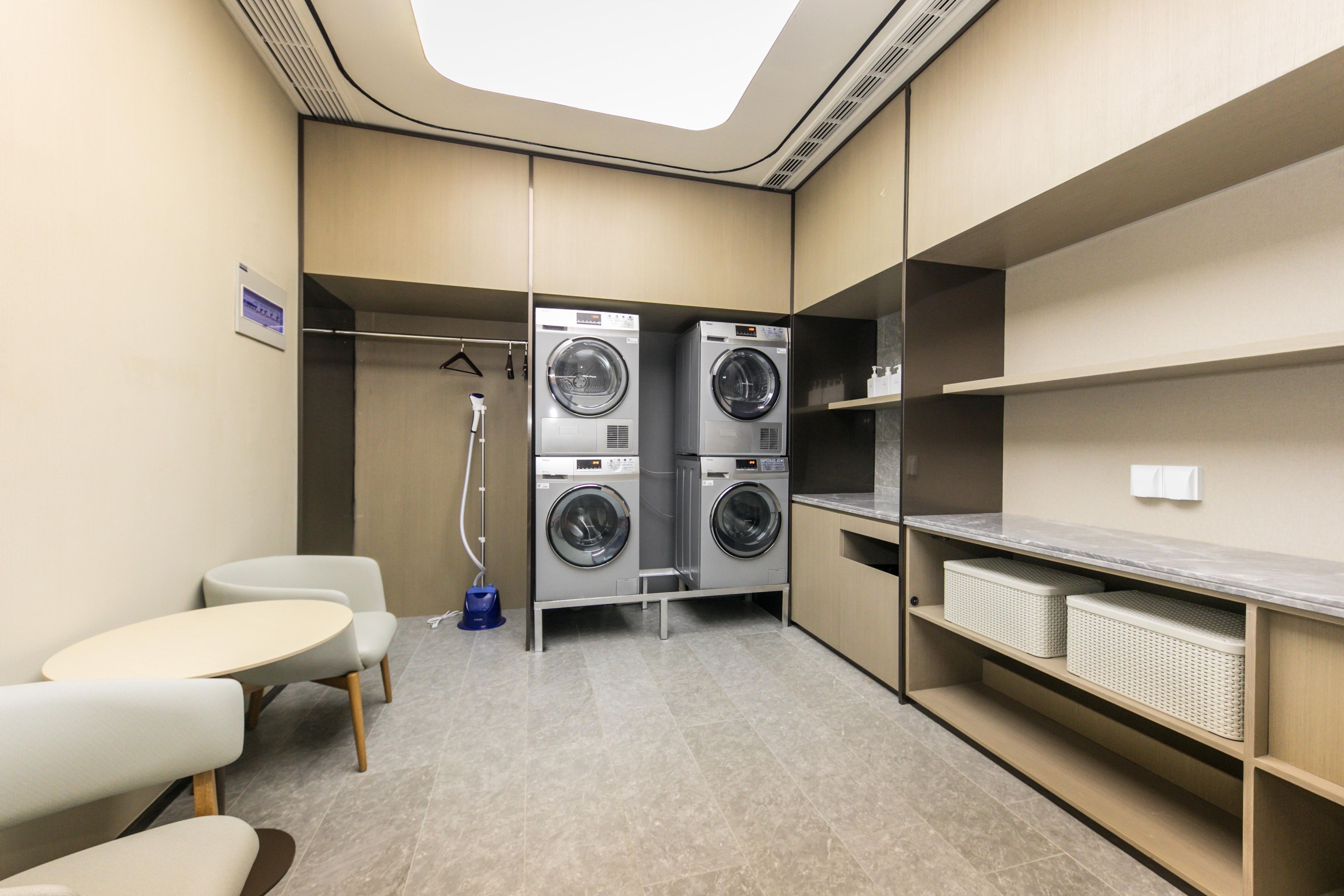 A compact hotel room with a built-in washer and dryer, a small seating area, and a view of the sky through the skylight.
