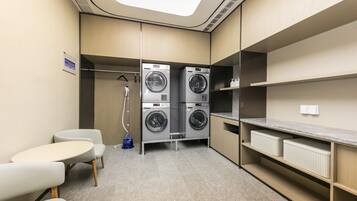 A compact hotel room with a built-in washer and dryer, a small seating area, and a view of the sky through the skylight.
