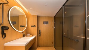 A hotel bathroom with a wooden vanity, a mirror with a light, a glass shower enclosure, and a door with a sign. - Ji Hotel (Nanjing)