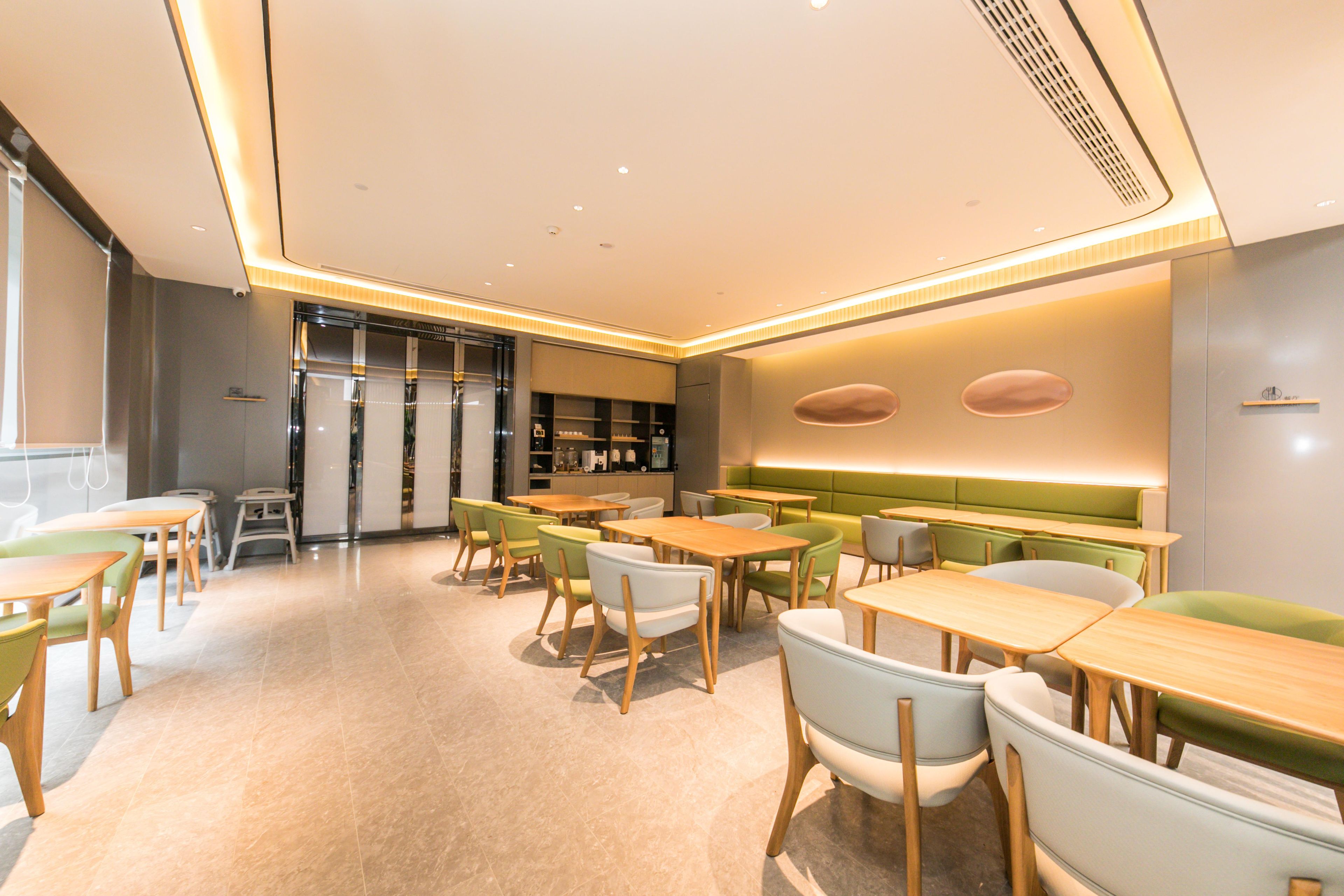 A modern dining area with tables and chairs, a counter, and a seating area with a green upholstered bench.
