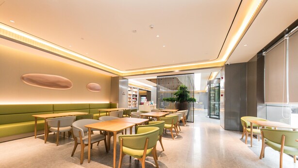 A modern restaurant interior with green seating, wooden tables, and a bright, well-lit ambiance. - Ji Hotel (Nanjing)