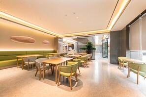 Un interior de restaurante moderno con asientos verdes, mesas de madera y un ambiente luminoso y acogedor.
