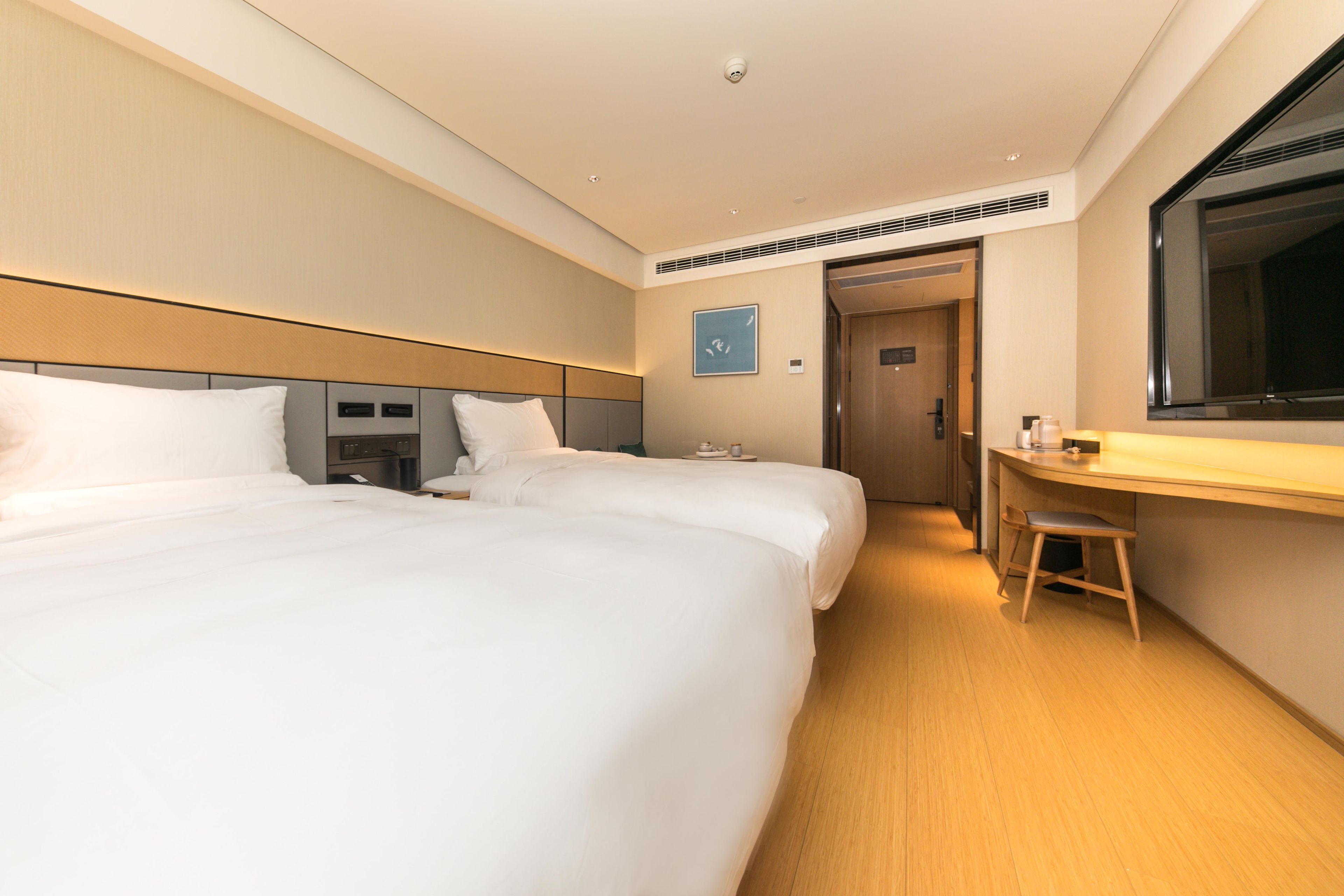 A hotel room with two beds, a desk, and a mirror.