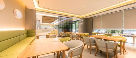 Un interior de restaurante moderno con asientos verdes, mesas de madera y vistas amplias por las ventanas.