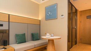 A modern hotel room with a sofa, a small round table, and a wall-mounted artwork. - Ji Hotel (Nanjing)