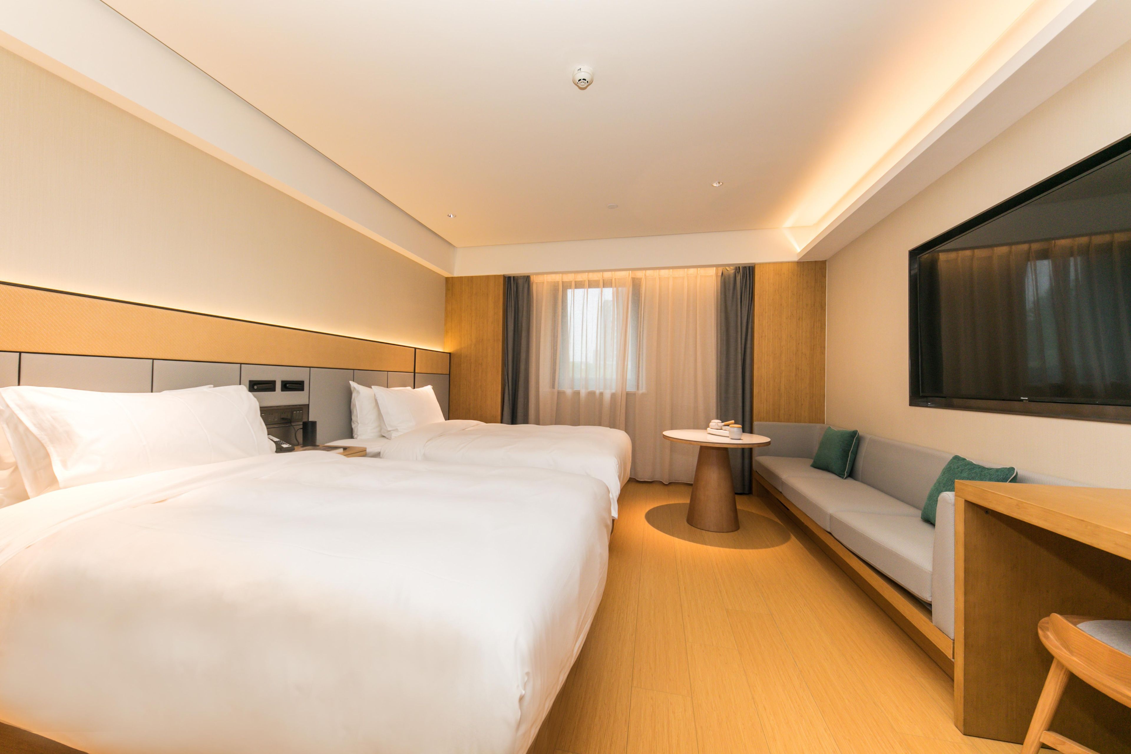 Een hotelkamer met een groot bed, een slaapbank, een tafeltje en een aan de muur bevestigde televisie.