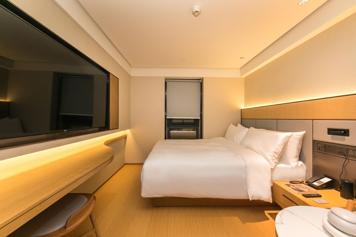 Una habitación de hotel moderna con una cama grande, una mesita de noche y un televisor.