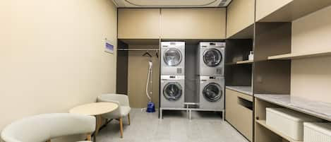 A compact laundry room with two washing machines, a small table, two chairs, and a ceiling light.