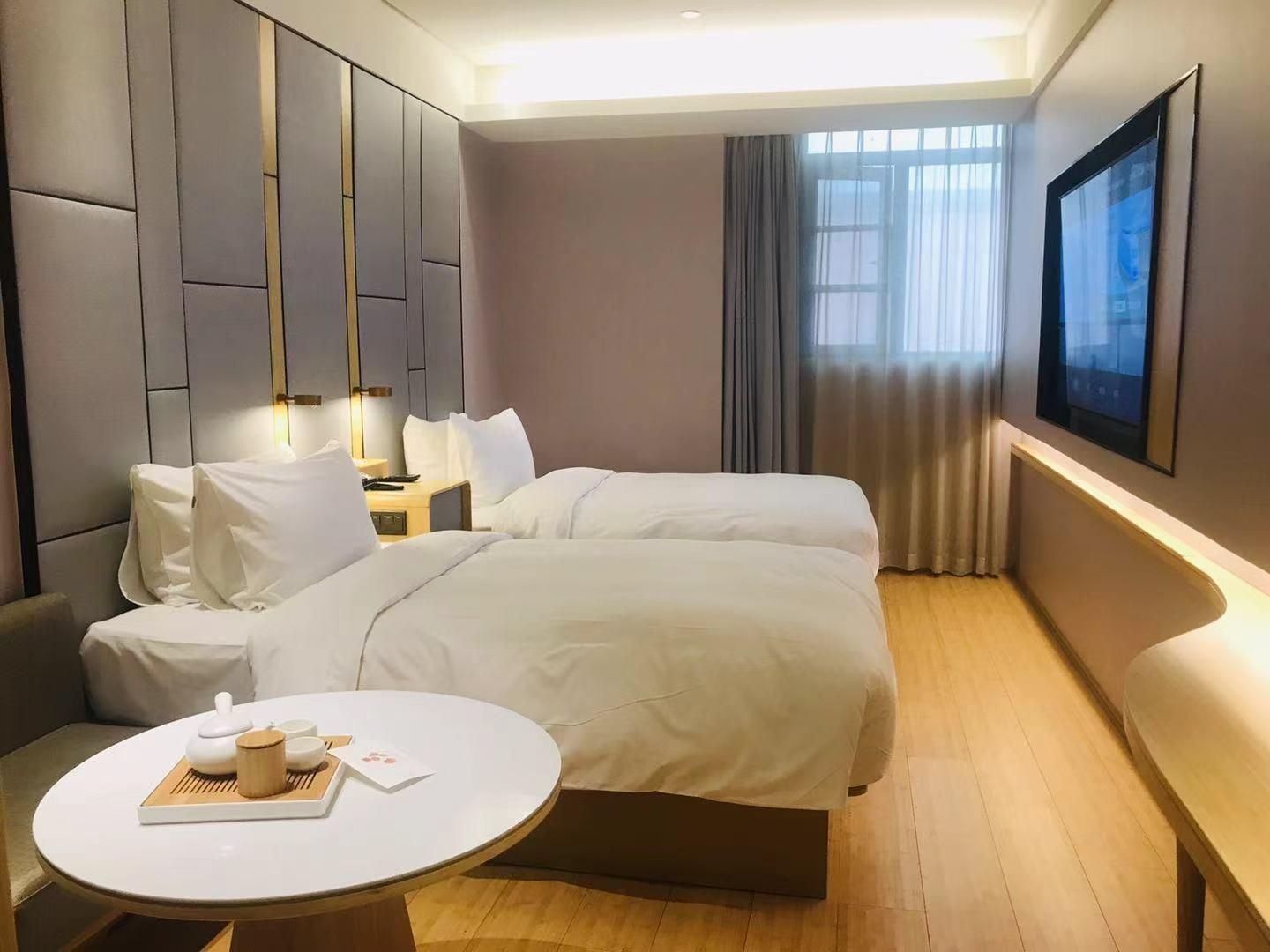 Ein Hotelzimmer mit Bett, Nachttisch mit Lampe, Stuhl, rundem Tisch mit Tablett und einem Fenster mit Vorhängen.