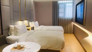 Ein Hotelzimmer mit Bett, Nachttisch mit Lampe, Stuhl, rundem Tisch mit Tablett und einem Fenster mit Vorhängen.