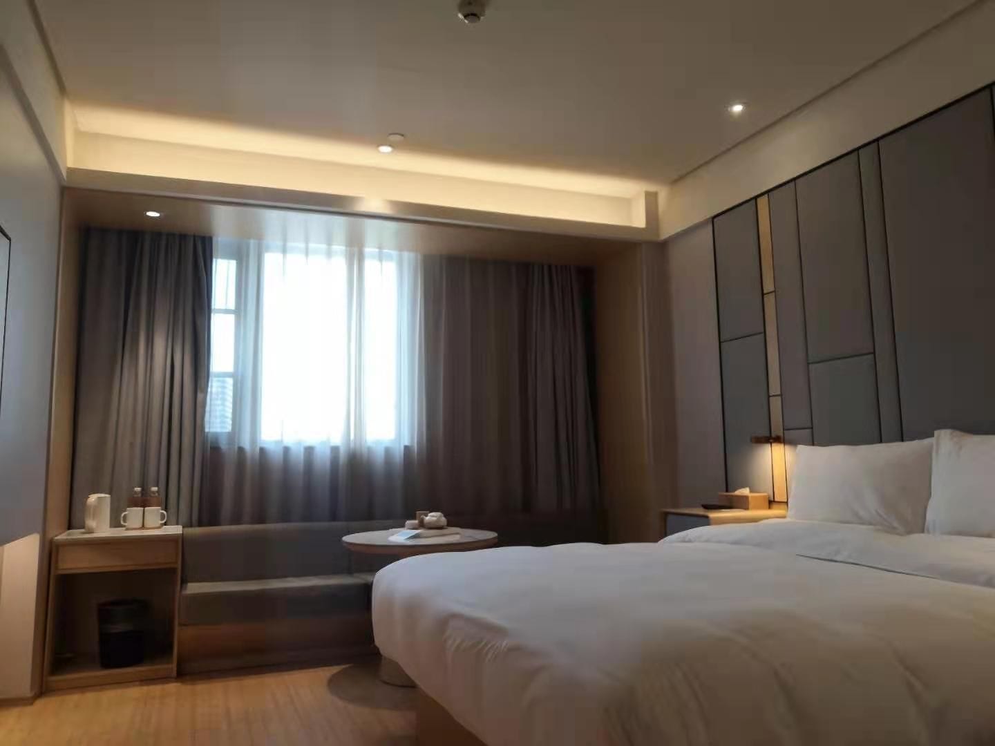 Een moderne hotelkamer met een groot bed, een nachtkastje, een klein rond tafeltje, een bank en een raam met gordijnen.