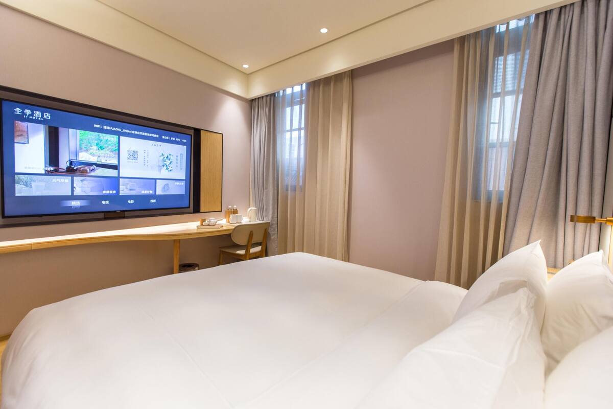 Una habitación de hotel con una cama grande, un escritorio con una computadora y un televisor mostrando la página web del hotel.