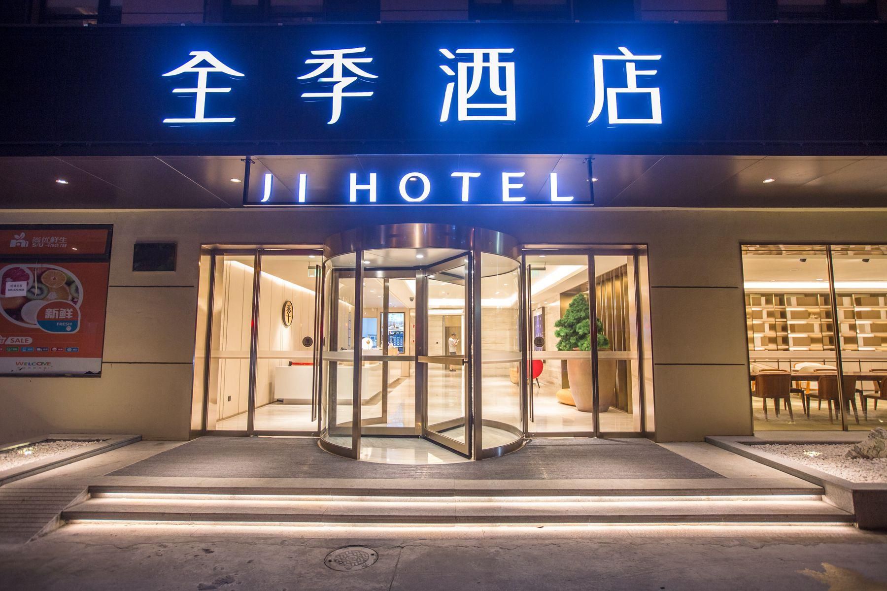 A hotel entrance with a revolving door, illuminated signage, and a visible interior with seating and a plant.
