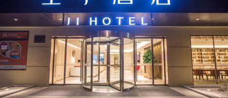A hotel entrance with a revolving door, illuminated signage, and a visible interior with seating and a plant.