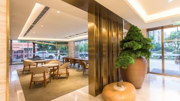 Een moderne hotel lobby met een zithoek, een grote potplant en uitzicht op de straat.