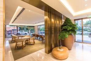 A modern hotel lobby with a seating area, a large potted plant, and a view of the street. - Ji Hotel (Shanghai)