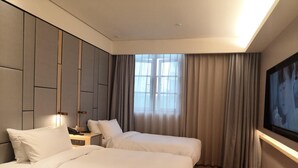Habitación de hotel con dos camas, una mesita de noche, un televisor y un ventanal con cortinas.