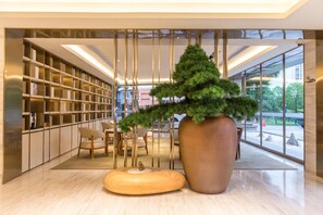 A modern lobby with a large bookshelf, a large potted tree, and a seating area.