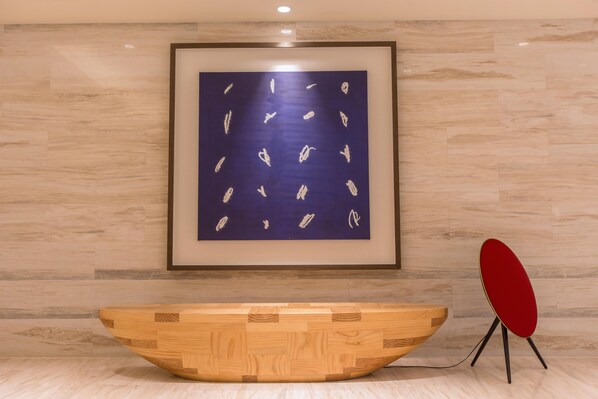 A reception area with a wooden console table, a framed abstract painting, and a red chair.