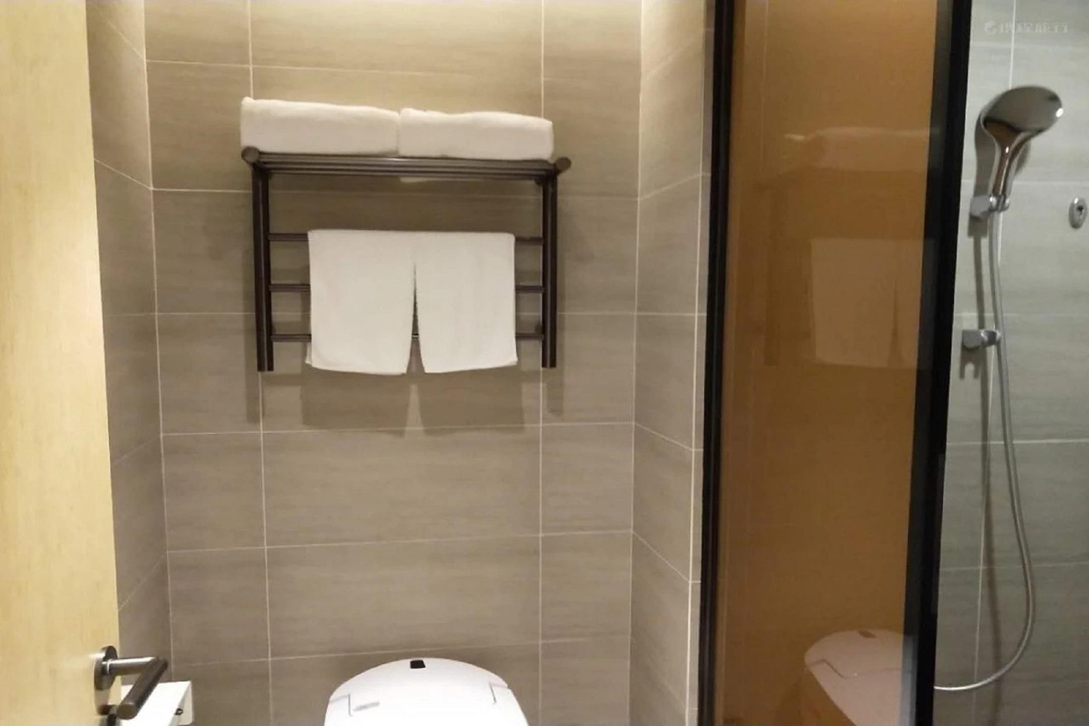 A bathroom with a toilet, a towel rack with towels, and a shower.