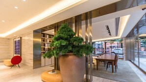 Un interior moderno con una planta grande en maceta, una silla roja y una zona de comedor con mesas y sillas.