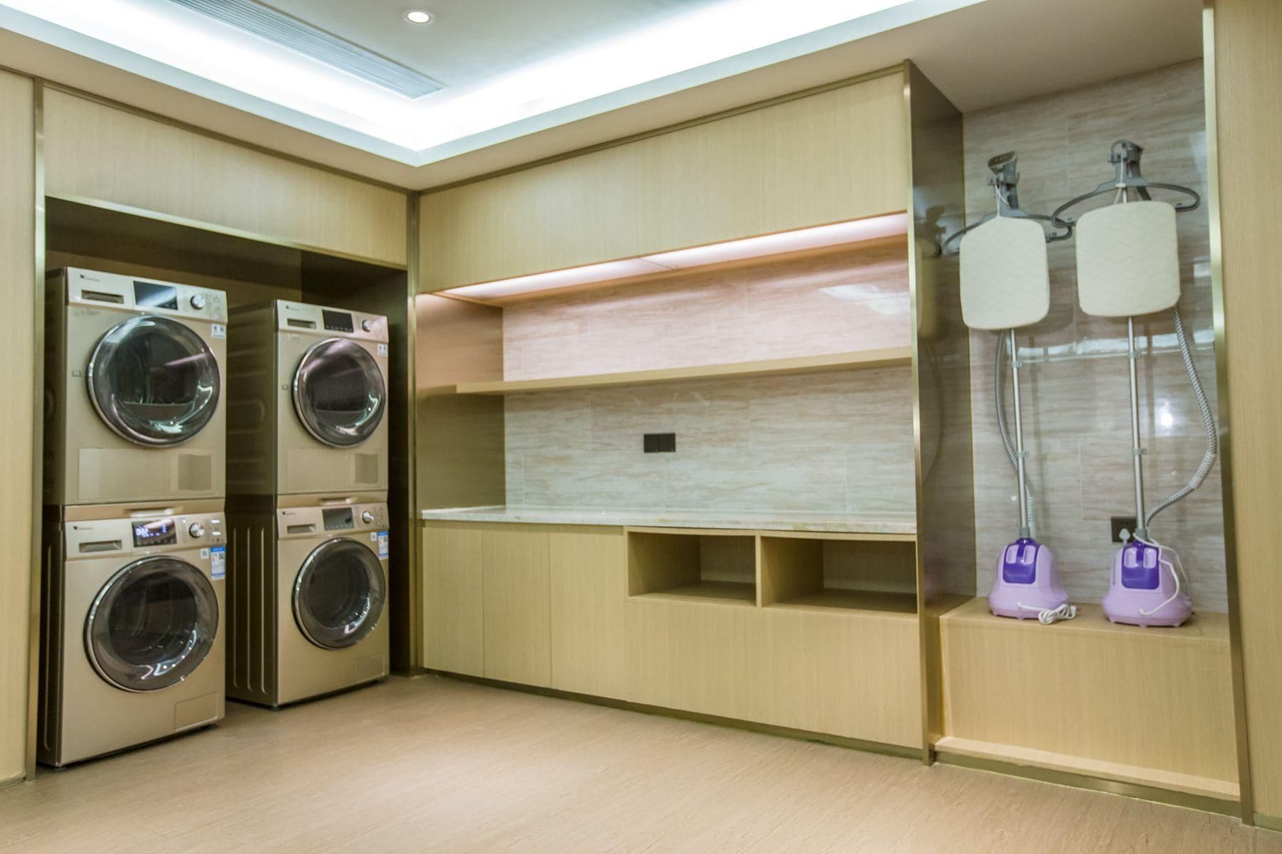 A laundry room with stacked washing machines, a shelf, and two purple water dispensers.