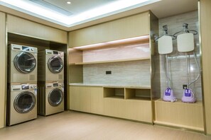 A laundry room with stacked washing machines, a shelf, and two purple water dispensers.