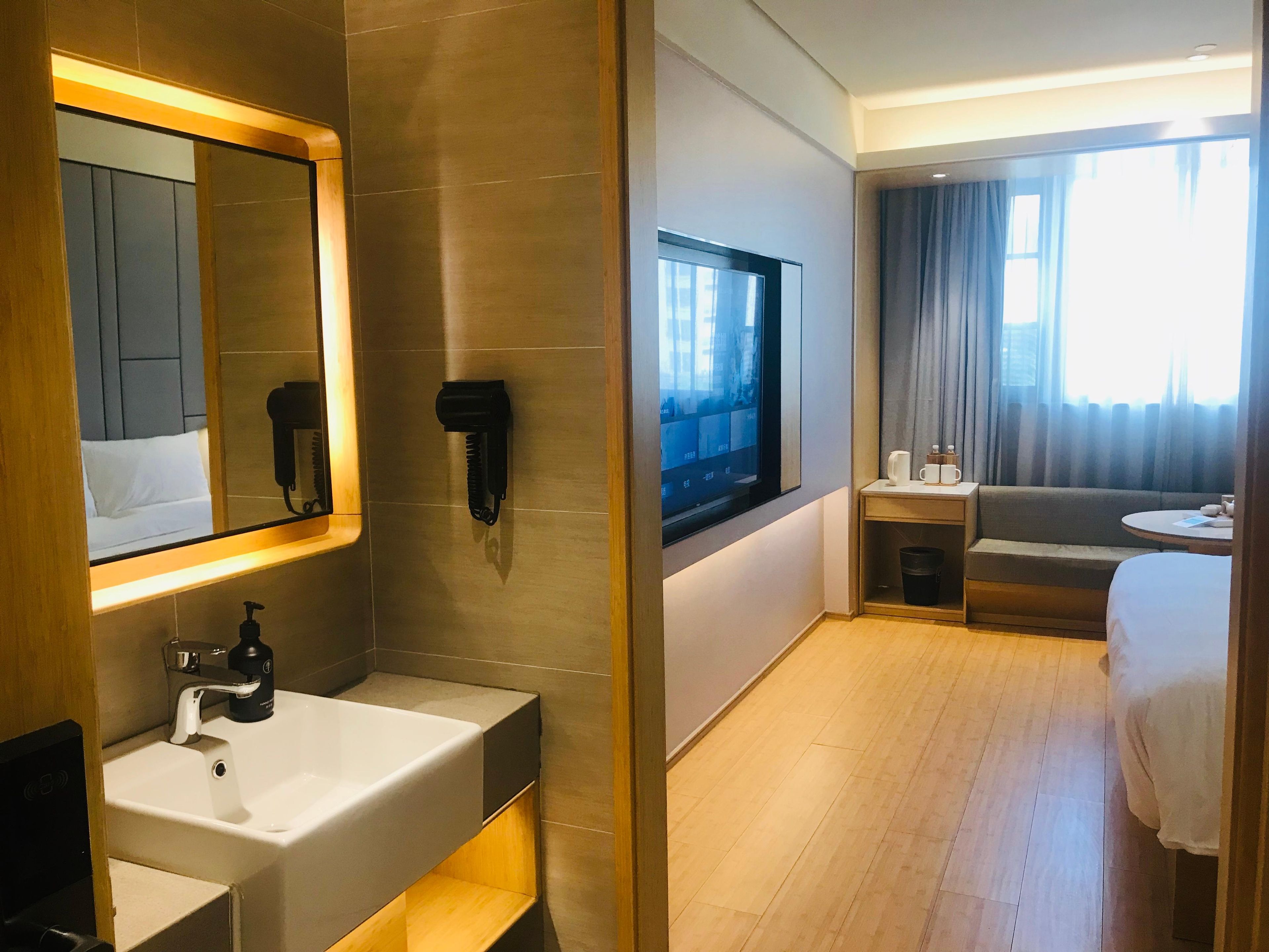 Habitación de hotel con un espejo grande, un lavamanos, un televisor, un sofá y una cama.