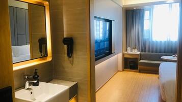 A hotel room with a large mirror, a sink, a television, a sofa, and a bed.