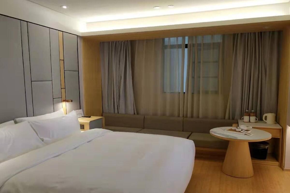 Una habitación de hotel con una cama grande, una mesita redonda, un sofá y una ventana con cortinas.