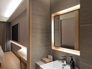 A modern bathroom with a large mirror, a white sink, and a handheld soap dispenser. - Ji Hotel (Shanghai)