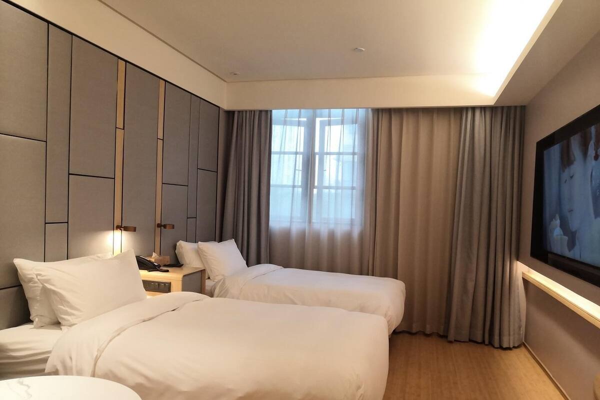 Habitación de hotel con dos camas, una mesita de noche, un televisor y un ventanal con cortinas.