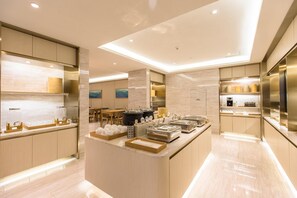 A modern kitchen with a central island, wooden cabinets, and a dining area in the background. - Ji Hotel (Shanghai)