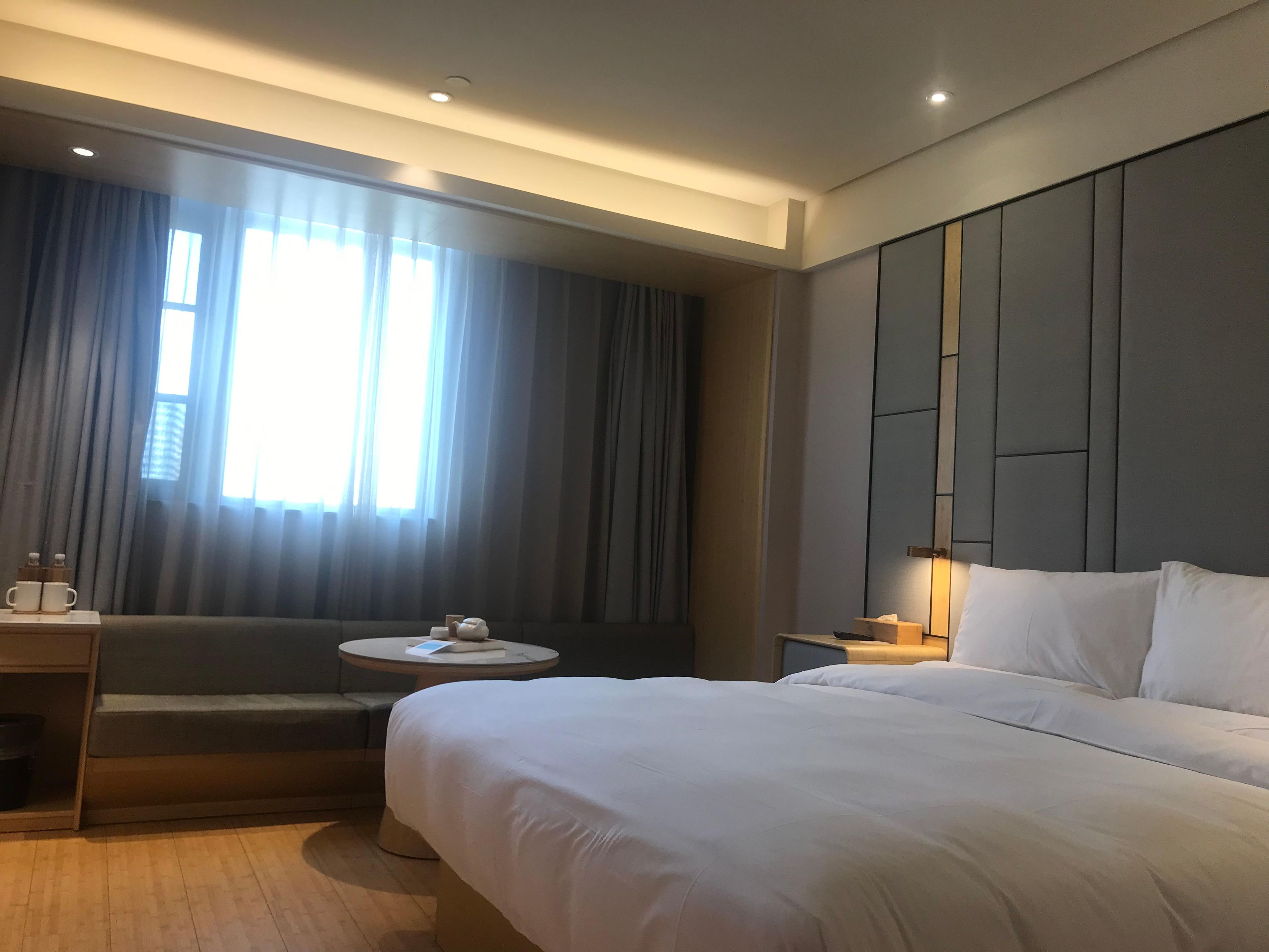 Ein Hotelzimmer mit einem großen Bett, einem Nachttisch, einem kleinen runden Tisch, einer Couch und einem Fenster mit Vorhängen.