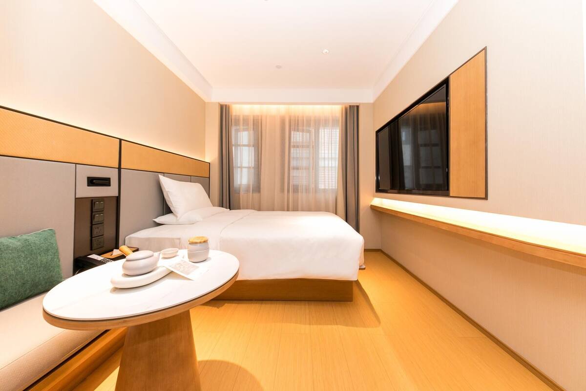 A hotel room with a bed, bedside table, and a TV mounted on the wall.