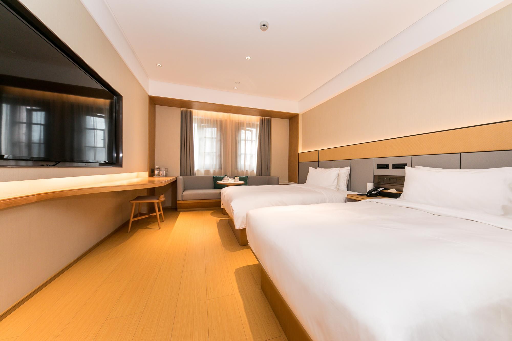 A hotel room with two beds, a desk, a chair, and a TV.