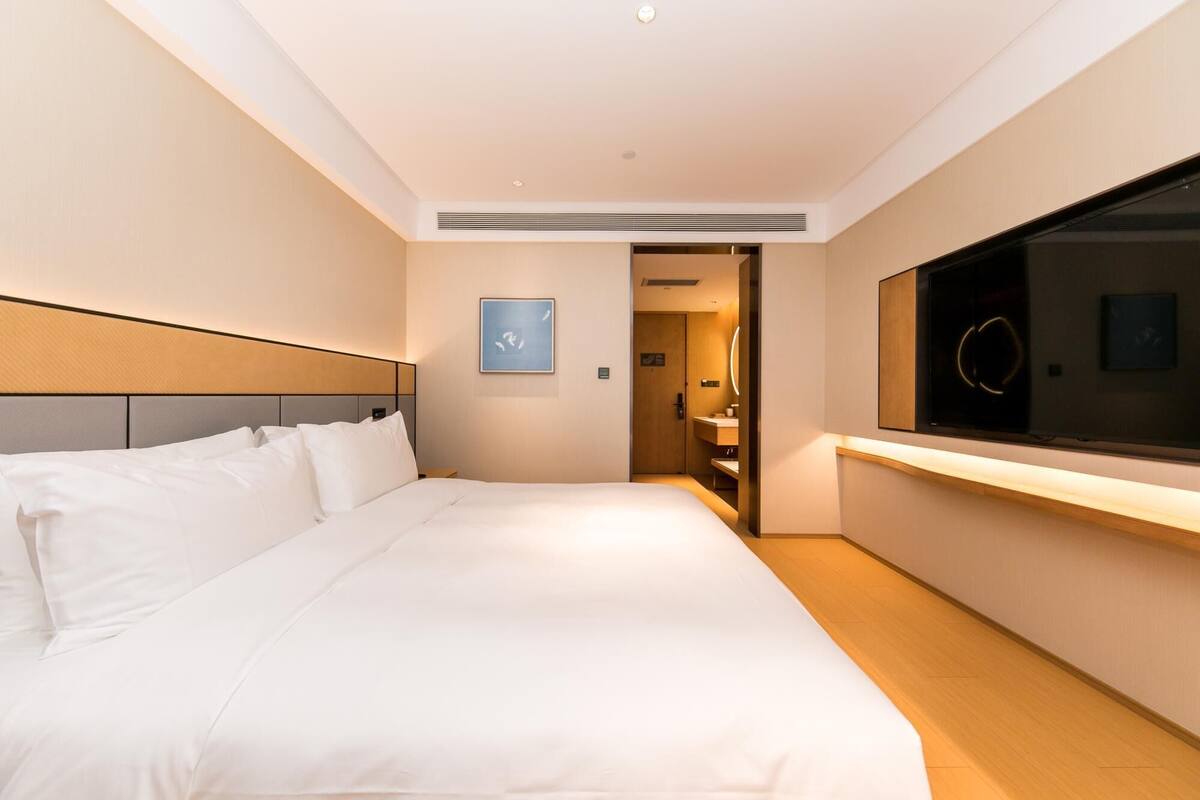 A hotel room with a large bed, a bedside table, a mirror, and a view of the bathroom.