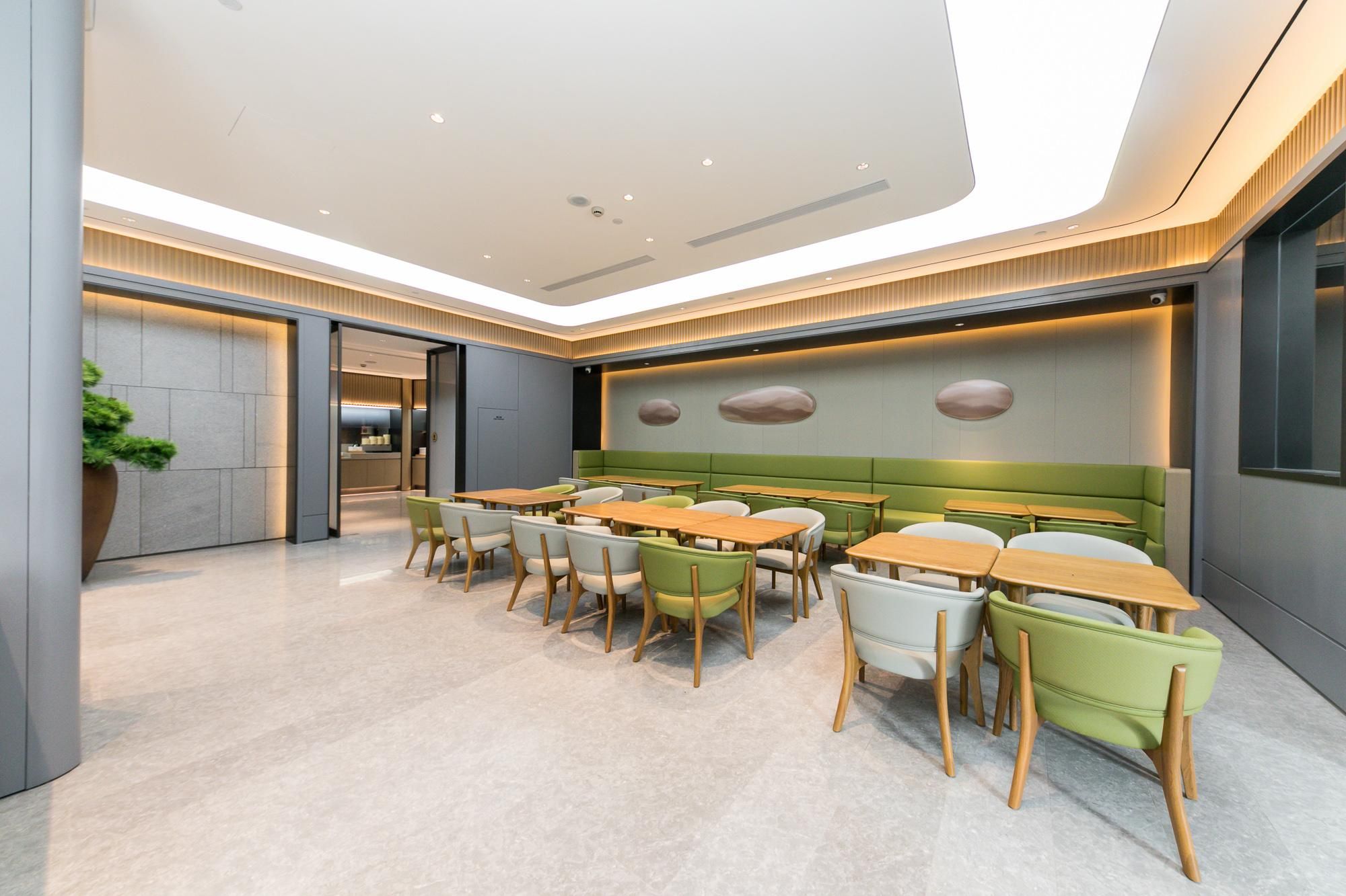 Un espace de restauration moderne avec plusieurs tables et chaises, une cuisine en arrière-plan et un plafond doté d’un éclairage encastré.