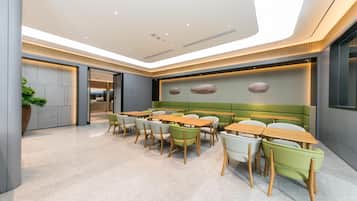 Un espace de restauration moderne avec plusieurs tables et chaises, une cuisine en arrière-plan et un plafond doté d’un éclairage encastré.