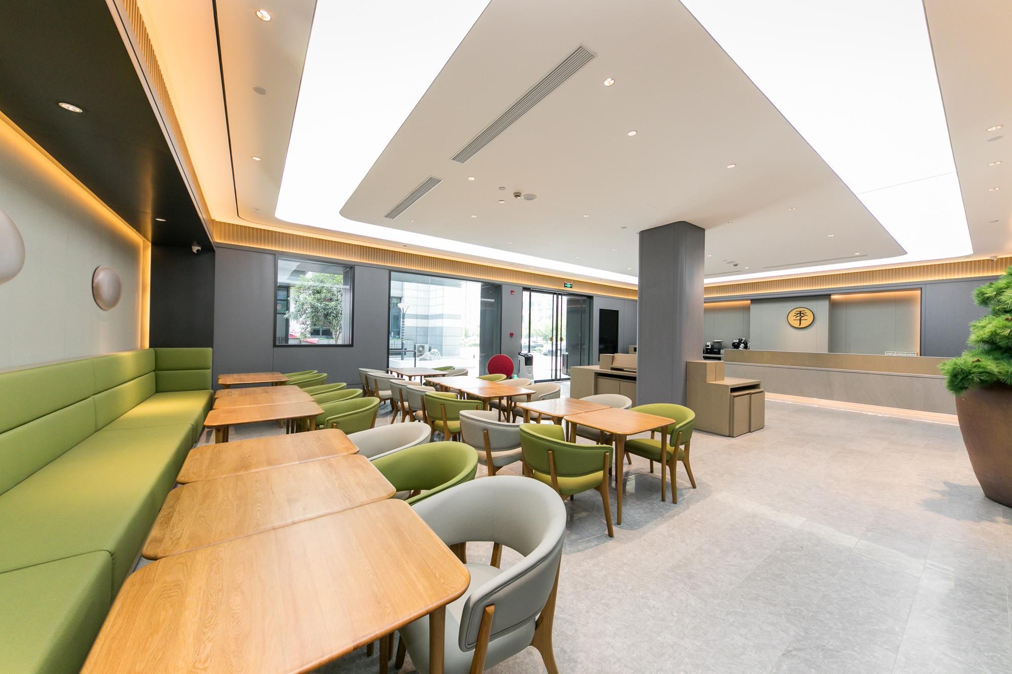 A modern hotel lobby with green seating, wooden tables, and a reception desk.
