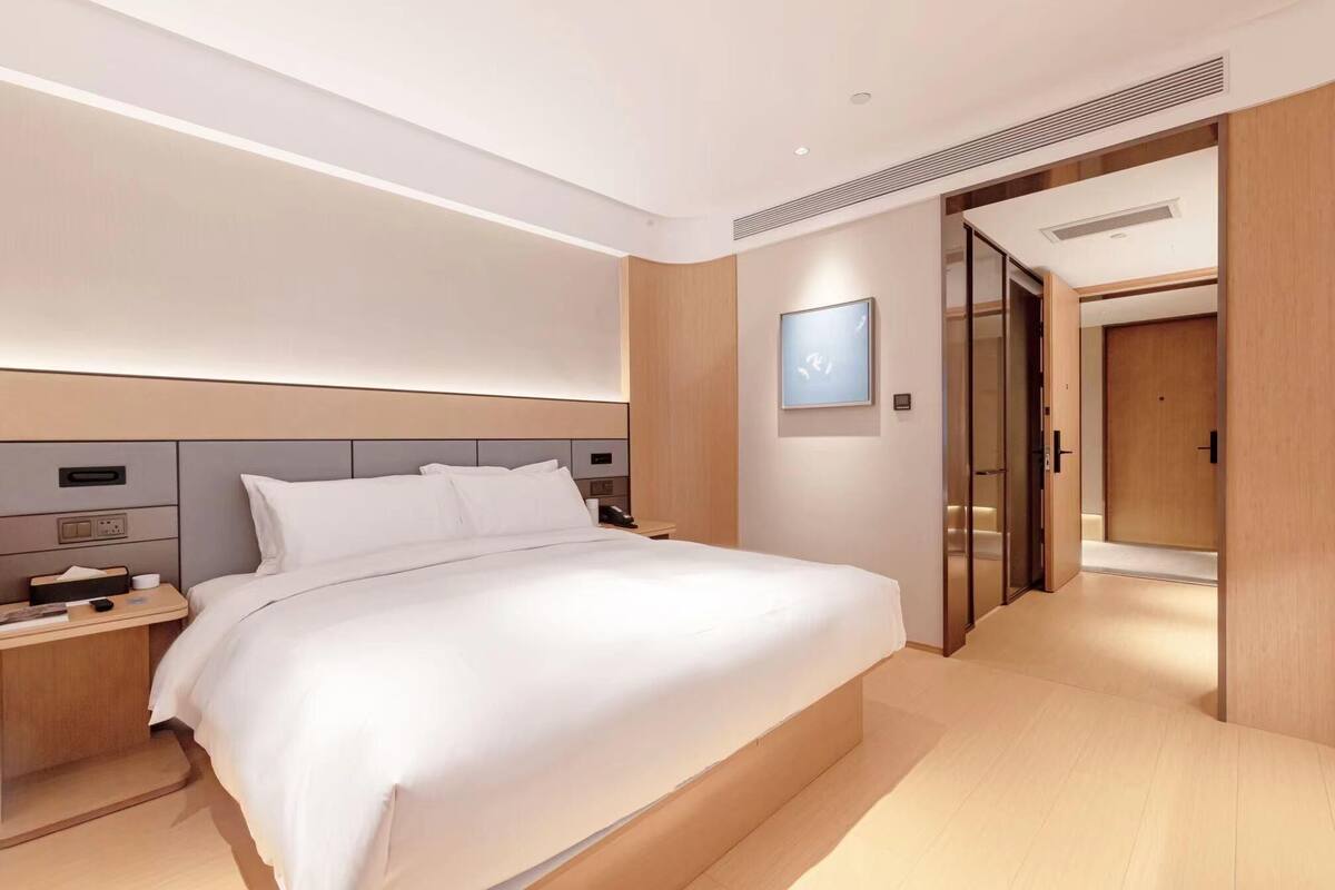 A modern hotel room with a large bed, bedside tables, a wall-mounted TV, and a wooden wardrobe.