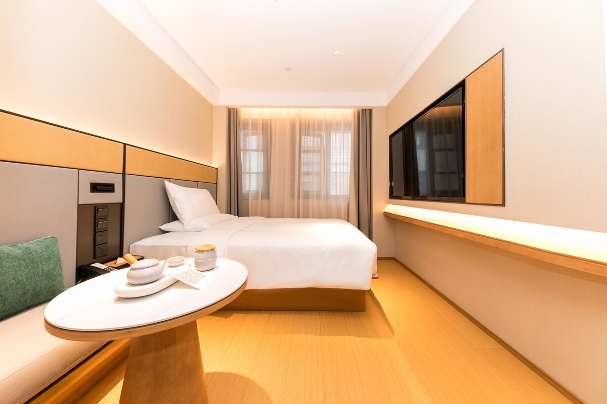 A hotel room with a bed, bedside table, and a TV mounted on the wall.