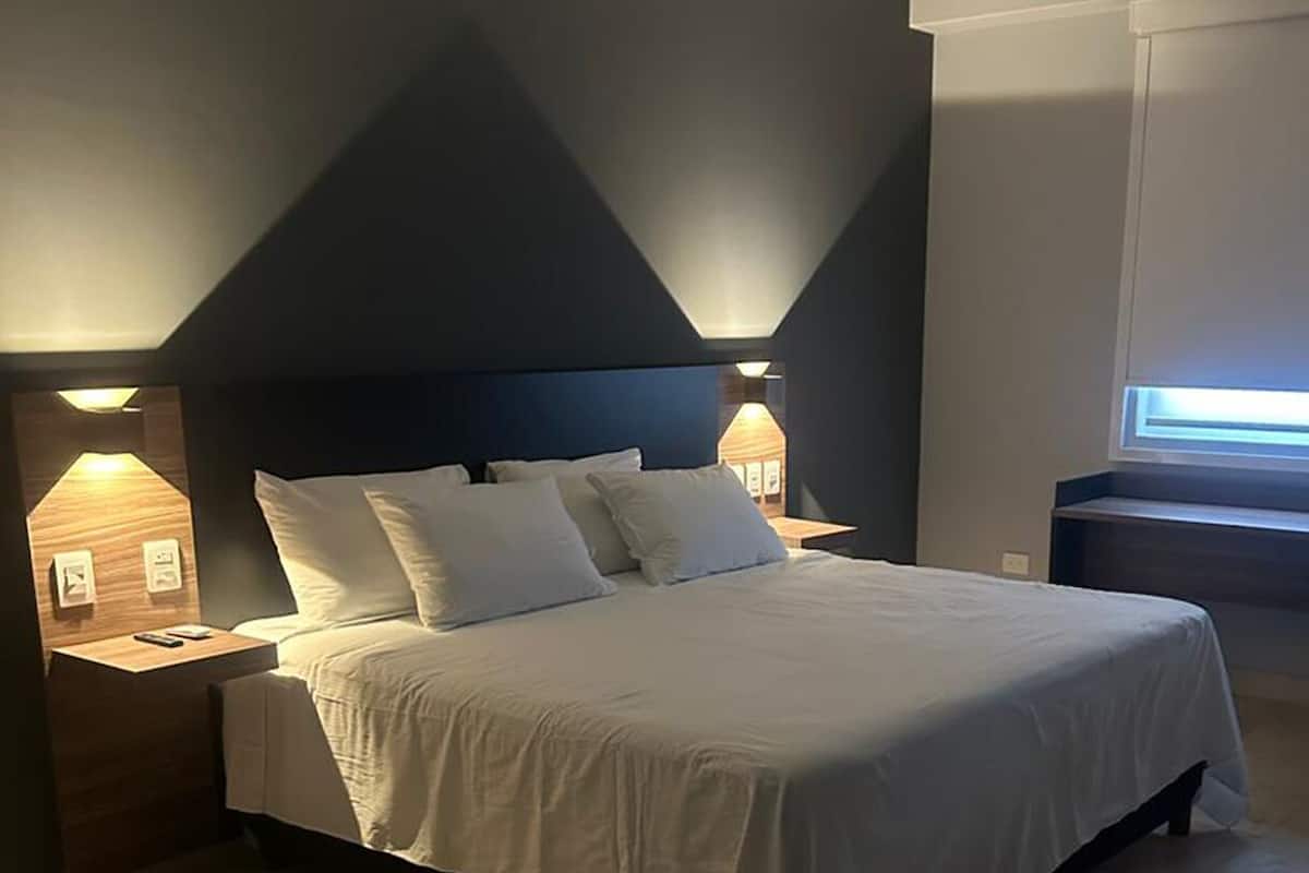 A modern bedroom with a bed, nightstands, and a window.