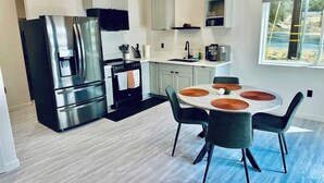 A modern kitchen with stainless steel appliances, a dining area with a round table and chairs, and a window with a view. - Sequoia Retreat: BBQ, Patio, Near National Park (Three Rivers)