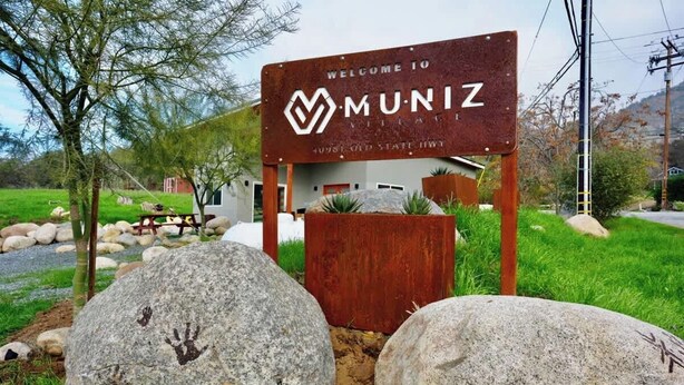 A welcome sign for Muniz Village with a rustic wooden structure, large rocks with handprints, and a grassy landscape. - Sequoia Retreat: BBQ, Patio, Near National Park (Three Rivers)